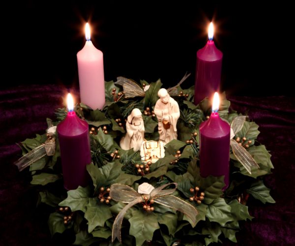 Three purple and one pink candle are set in a leafy wreath with small figurines depicting the Holy Family in the centre