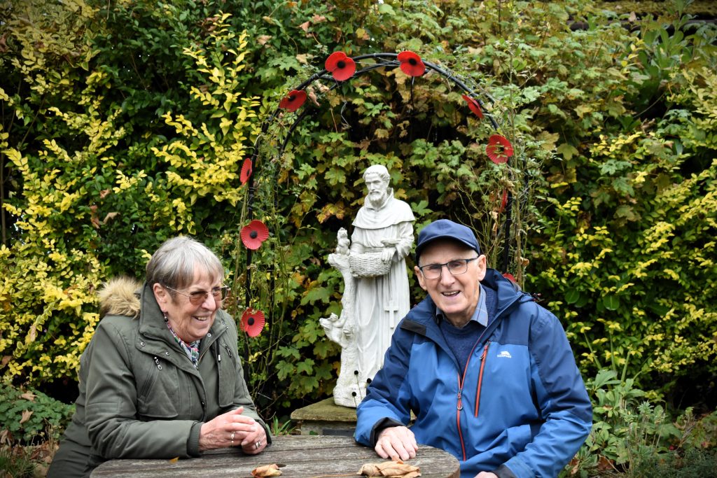 Pauline chats with another volunteer in front of a statute of St Francis of Assisi surrounded by hedges and trees