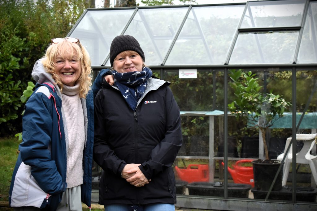 Two female volunteers enjoying a laugh whilst working in front of the greenhouse