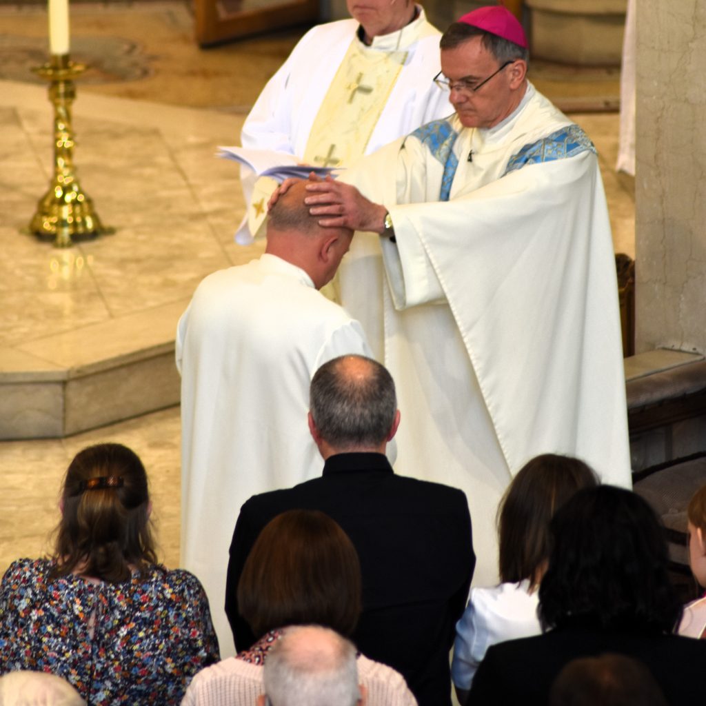 Bishop John places his hands on Deacon Lee's head during ordination, as family members and friends look on. 
