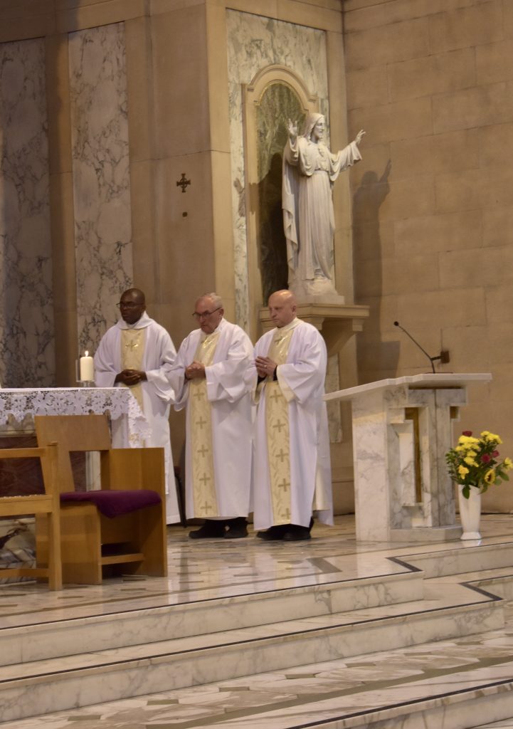 Deacon Davie Nalikata, Deacon John Walsh, and Deacon Lee Davies stand to the side of the altar