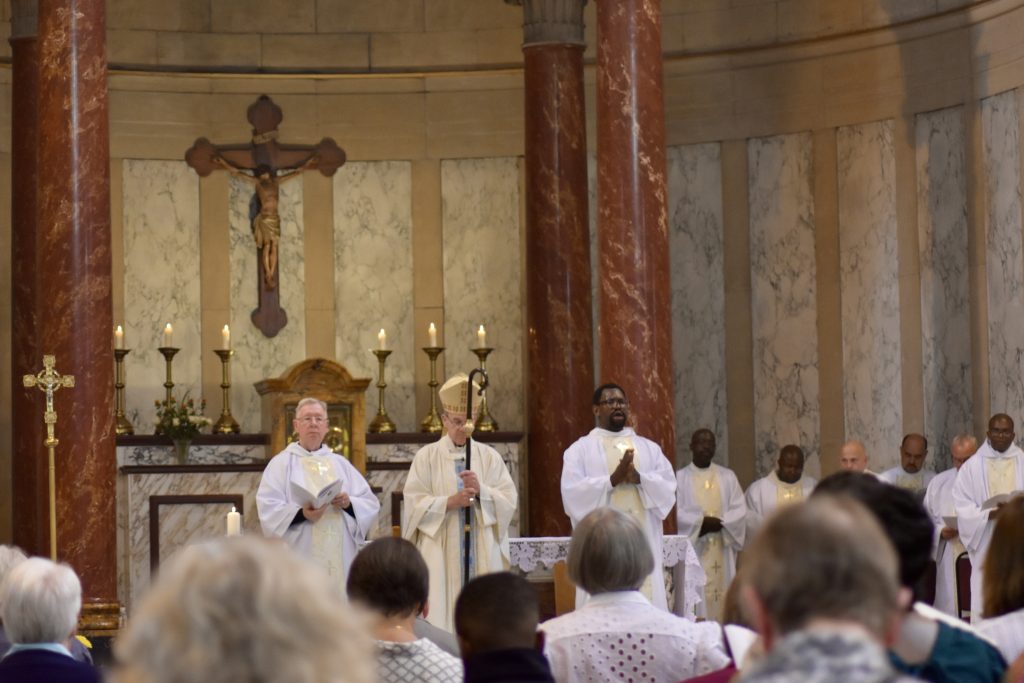 Deacon Stephen stands with Bishop John and Deacon Patrick Tifu in front of the altar before the congregation