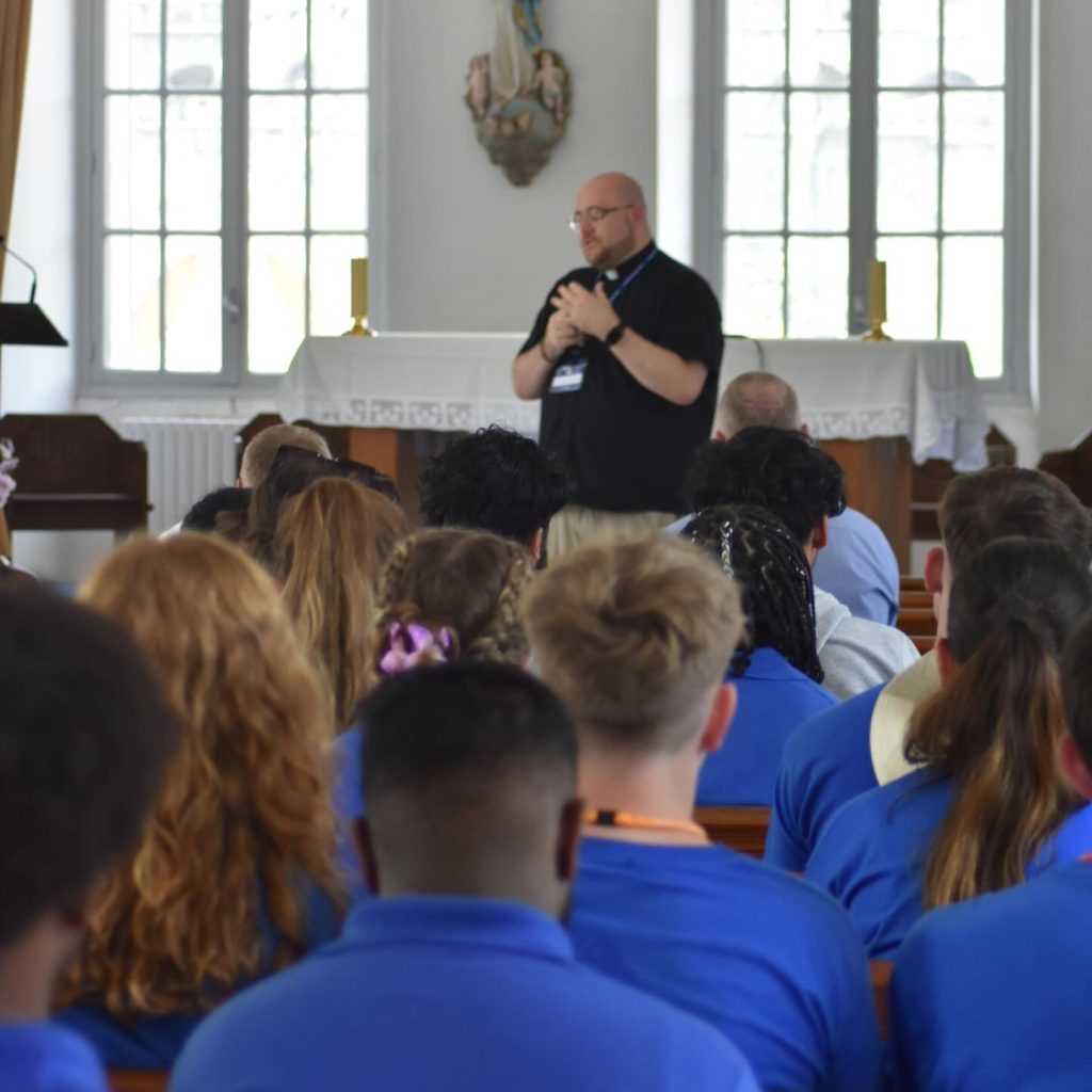 Deacon Luke speaks to a group of young pilgrims in blue t-shirts