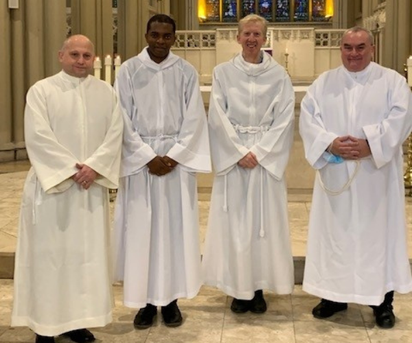 Four deacons stand in front of the altar in Salford Cathedral, dressed in white vestments, on their ordination day