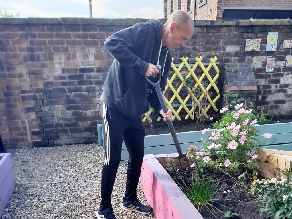 A person in dark clothing is gardening an accessible planter in a walled area