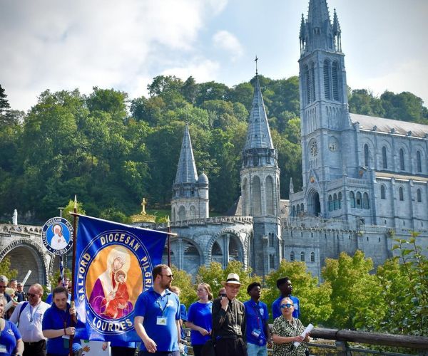 Pilgrims with our diocesan Lourdes banner walk in procession with the basilica in the background