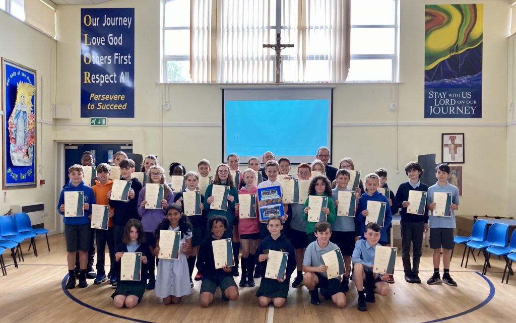 School children stand for a group photo holding certificates in their school hall