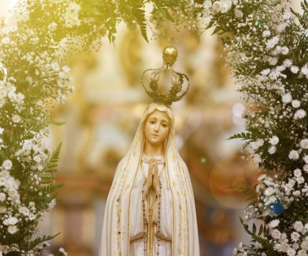 Statue of Our Lady of Fatima, dressed in white and gold trim, wearing a golden crown and surrounded by flowers.