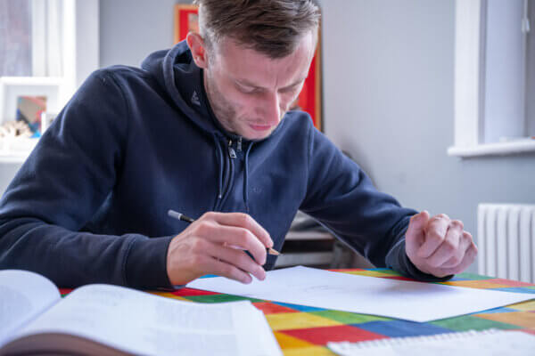 A person in a dark hoody holds a pen and completes paperwork