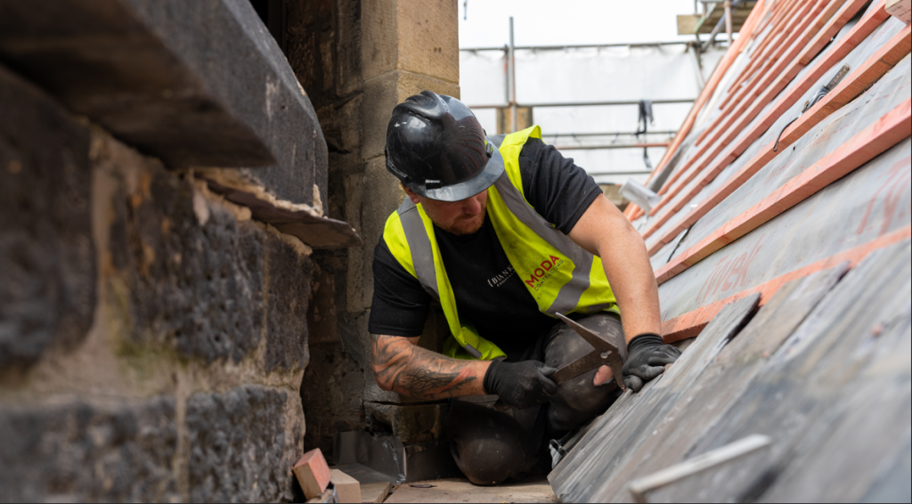 A worked in hi-vis and a hard hat works on restoring the slate tiles on the roof