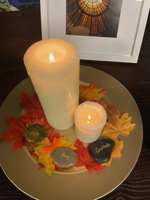 St Catherine of Siena's Synod table incudes a framed photo of a dove, representing the Holy Spirit, a gold-coloured plate covered in orange leaves, with two lit pillar candles and three stones saying "hope", "pray", and "gratitude".