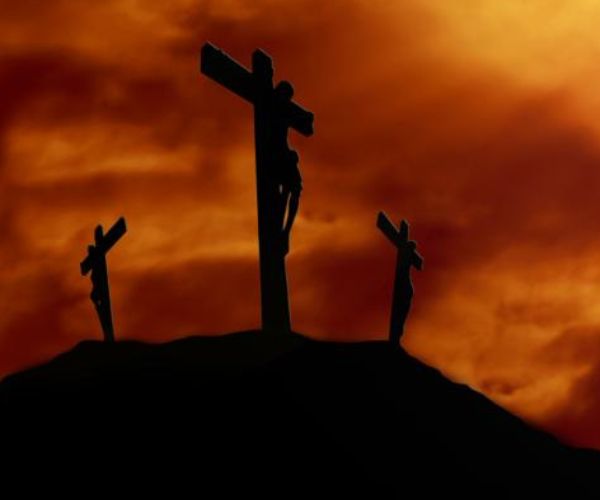Silhouette of Calvary with three crosses against the orange-red colour of the sky