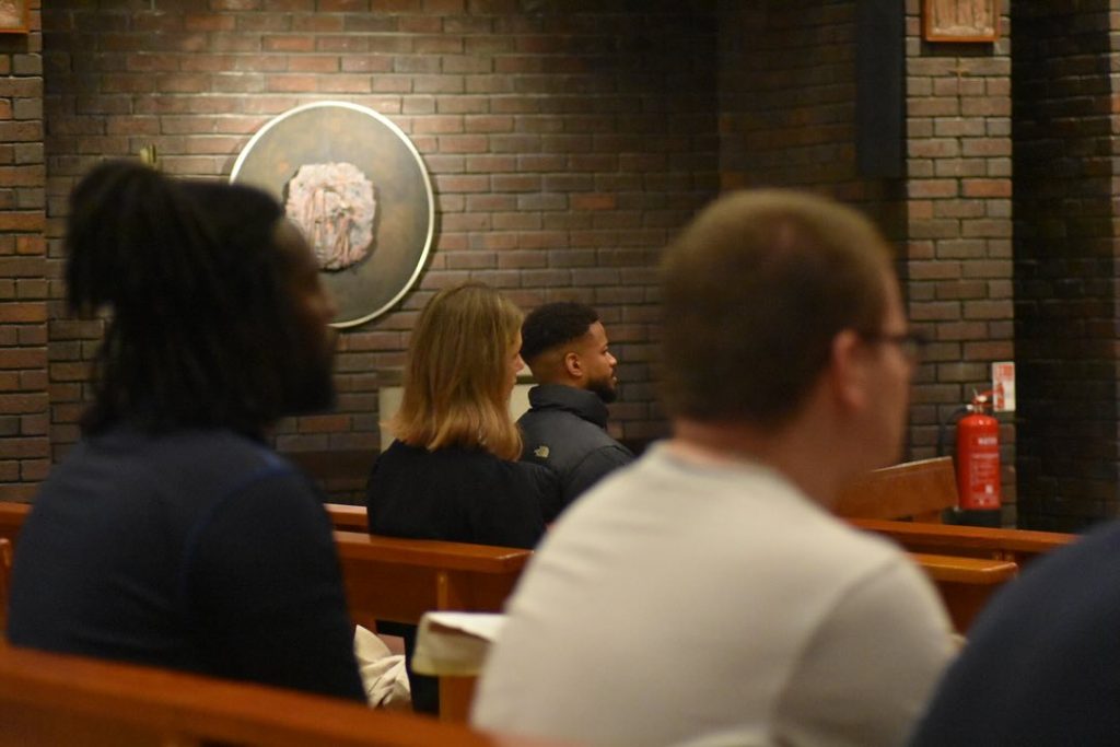 Young adults sit in the wooden pews of a grey-brick church