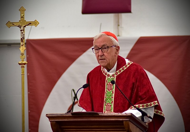 Cardinal Nichols in red vestments preaches from the lectern next to a golden crucifix