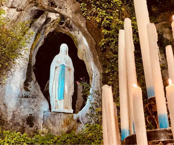 Statue of Our Lady in the grotto at Massabielle, Lourdes, with tall white candles to the right-hand side.