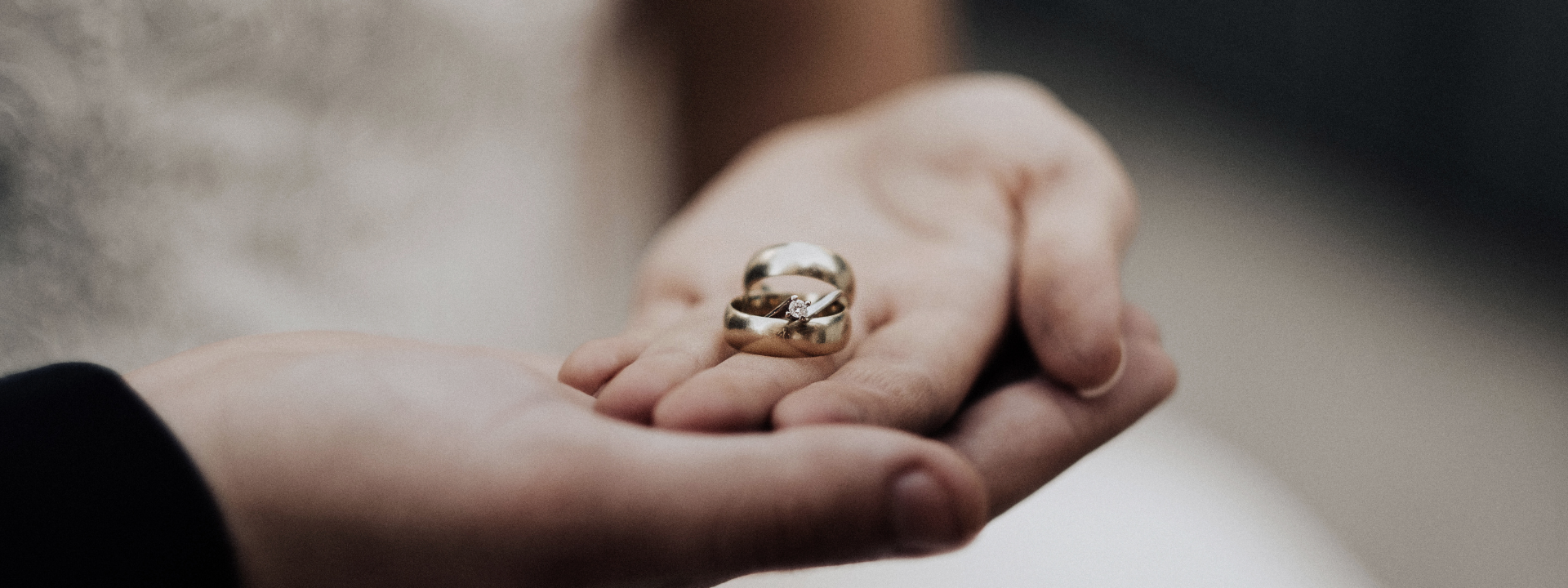 A bride and grooms hands are joined, palms facing up and holding two rings
