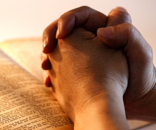 Hands clasped together in prayer on top of an open Bible