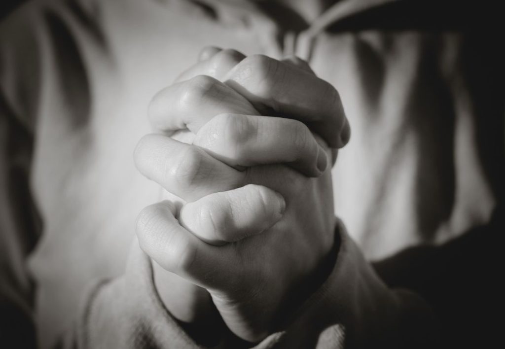 Greyscale image of a person with hands clasped in prayer