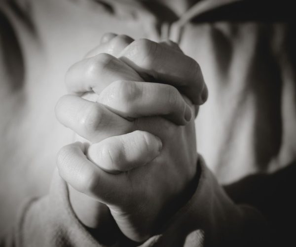 Greyscale image of a person with hands clasped in prayer