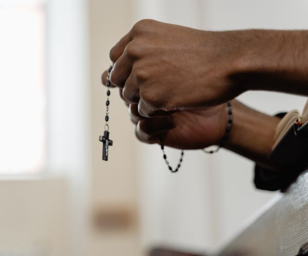 Photo showing hands holding a Rosary in prayer against a blurred out background of a church