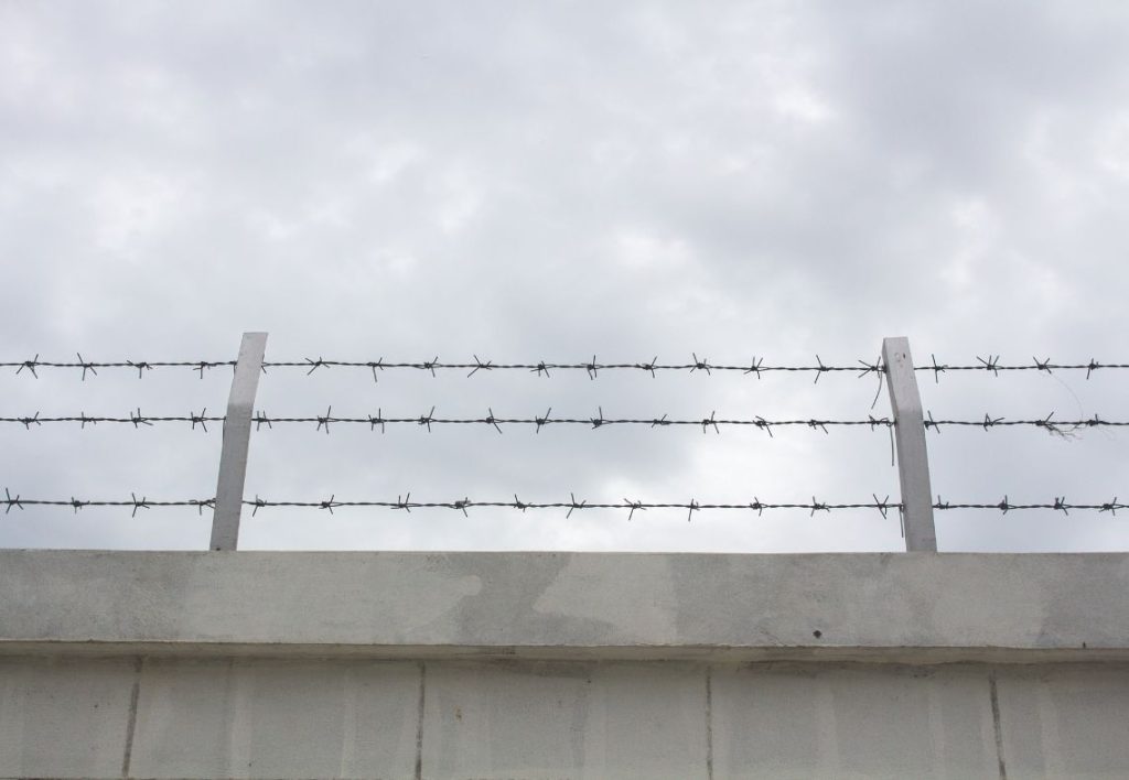 A grey wall topped with barbed wire against the backdrop of a cloudy sky